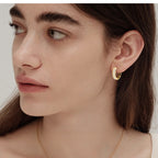 Gold hoop earrings worn on a woman's ear in natural light